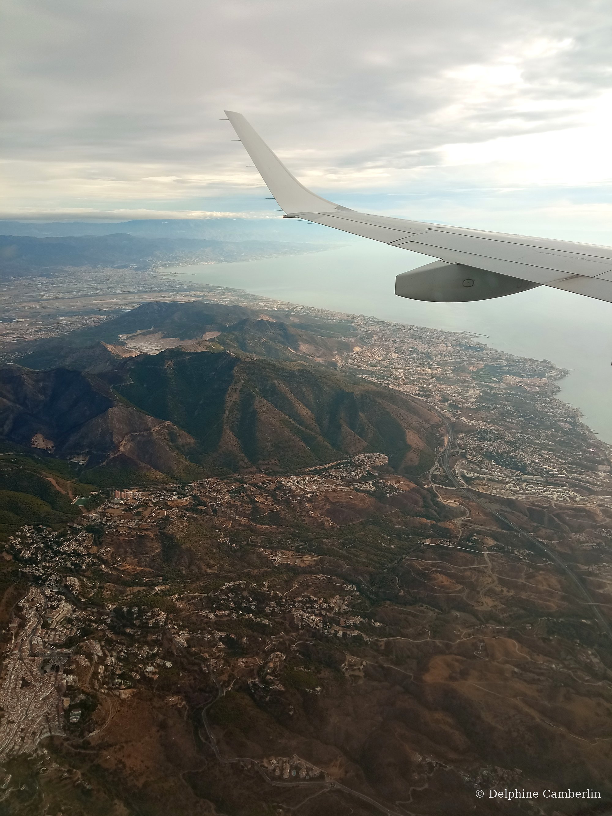 Plane wing over Spain coast — economy vs business class carbon footprint