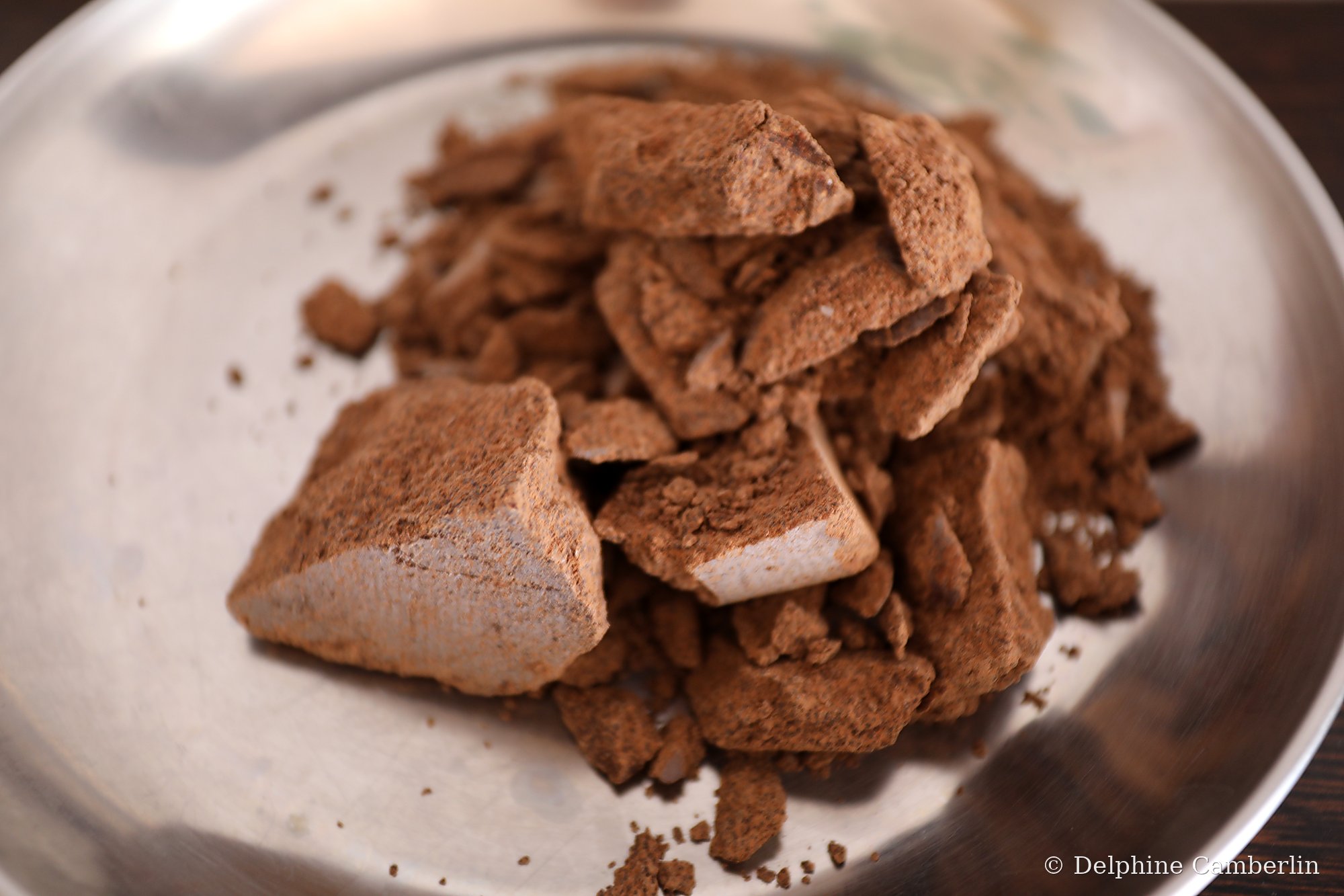 Crumbled raw cacao paste on a steel plate — ceremonial preparation